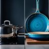 A striking comparison between ceramic and stainless steel cookware in a modern kitchen setting. On one side, a sleek stainless steel pan with a matching pot, showcasing the durability and professional feel of the material. On the other side, a beautiful ceramic skillet with a vibrant, swirling blue glaze, exhibiting the elegance and warmth of the material. The background features modern appliances and kitchen tools, highlighting the versatility and compatibility of both materials in a contemporary kitchen.