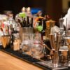 a well-stocked bar with a variety of equipment and tools. The countertop is filled withvariousglasses, liquor bottles, and a mix of modern and vintage tools.